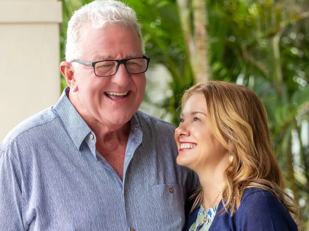 An older man and a woman smiling together outdoors, representing patient care and supportive relationships at the clinic.